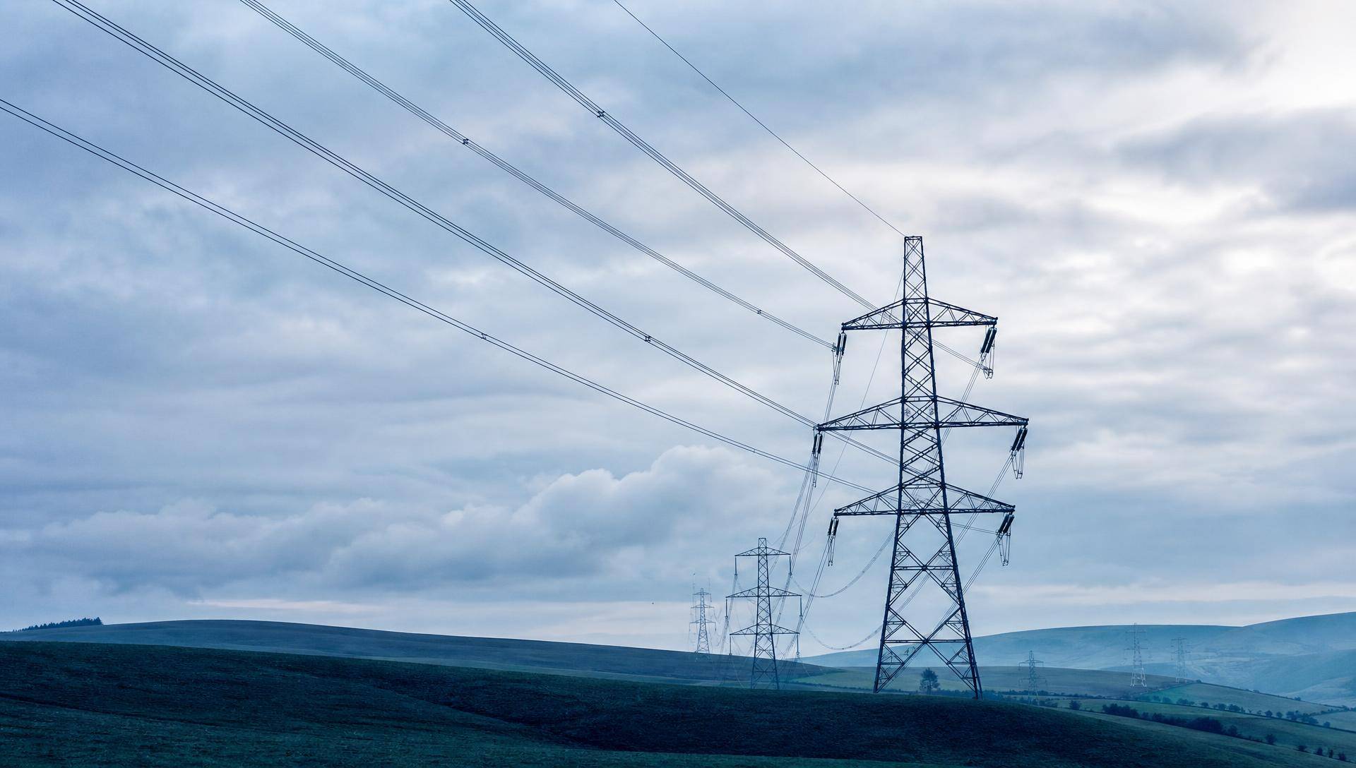 An electricity transmission pylon on open moorland, overhead lines running across a clouded sky.